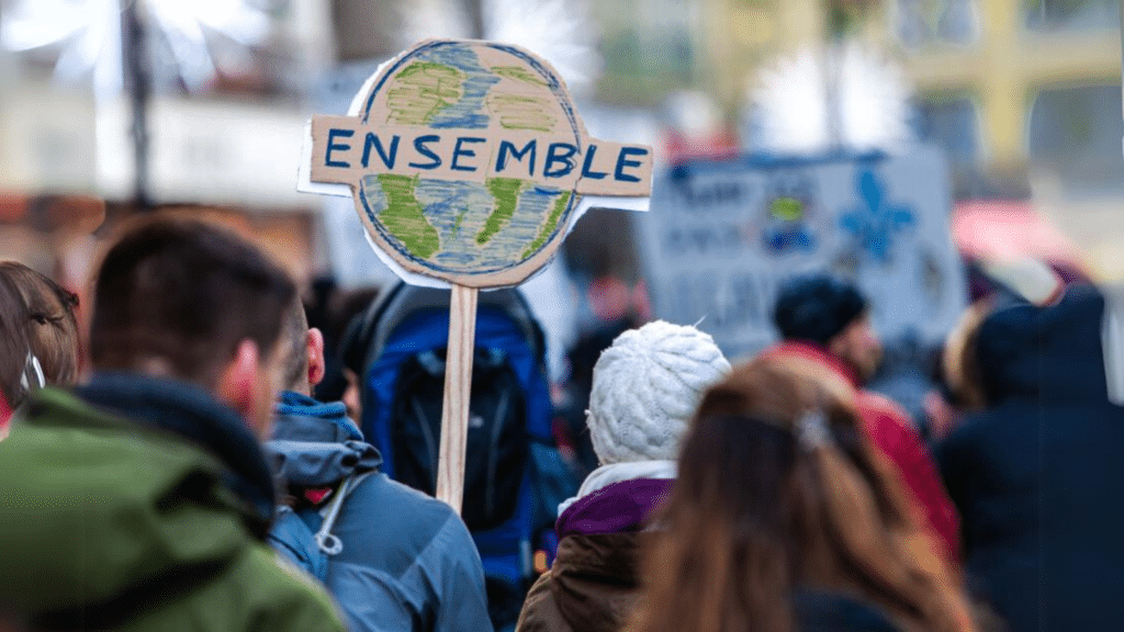 A street protest with focus on a handmade sign of the Earth with 'emsemble' written across it