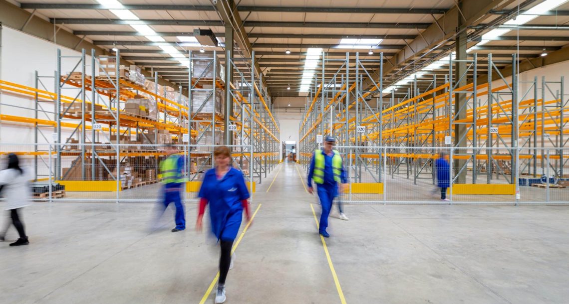 Warehouse with workers dresses in blue jumpsuits and high vis jackets walking around