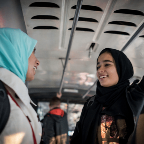 Two young women in headscarves talk on a bus