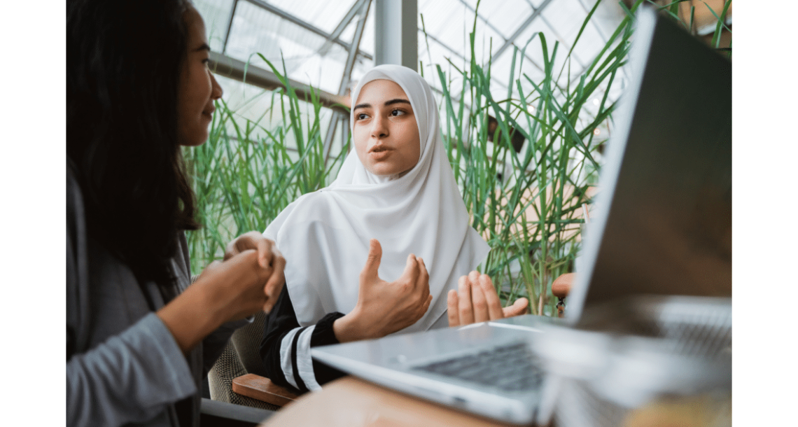 Muslim women explaining sitting next to friend with laptop in front of them