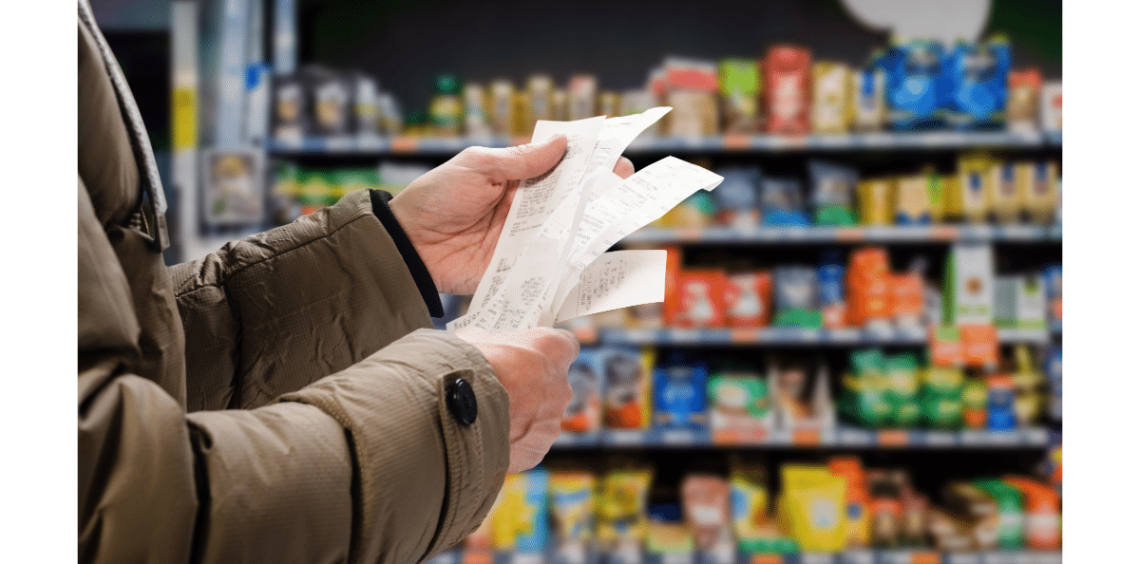 Hands holding multiple receipts with a grocery store in the background